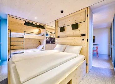 Gemütliches Familienapartment mit Doppelbett, Etagenbett und moderner Küchenzeile aus hellem Holz.