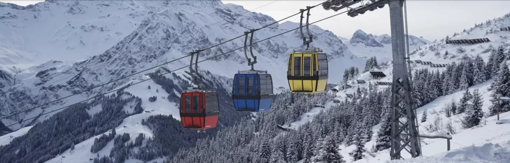 Bunte Gondeln einer Seilbahn bei winterlicher Berglandschaft in Tschentenalp, Adelboden, Talstation direkt hinter dem Apart Hotel