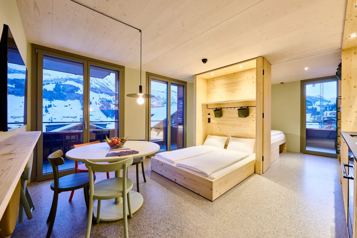 Gemütliches Apartment mit Holzmöbeln, Doppelbett, Esstisch und Panoramablick auf die verschneiten Berge.